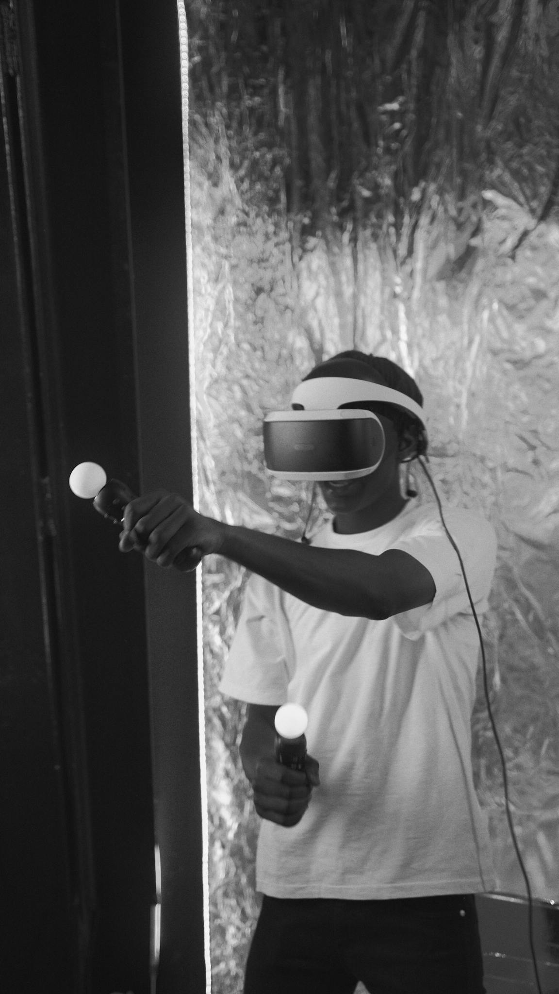 A person enjoying virtual reality gaming with controllers, captured in black and white.