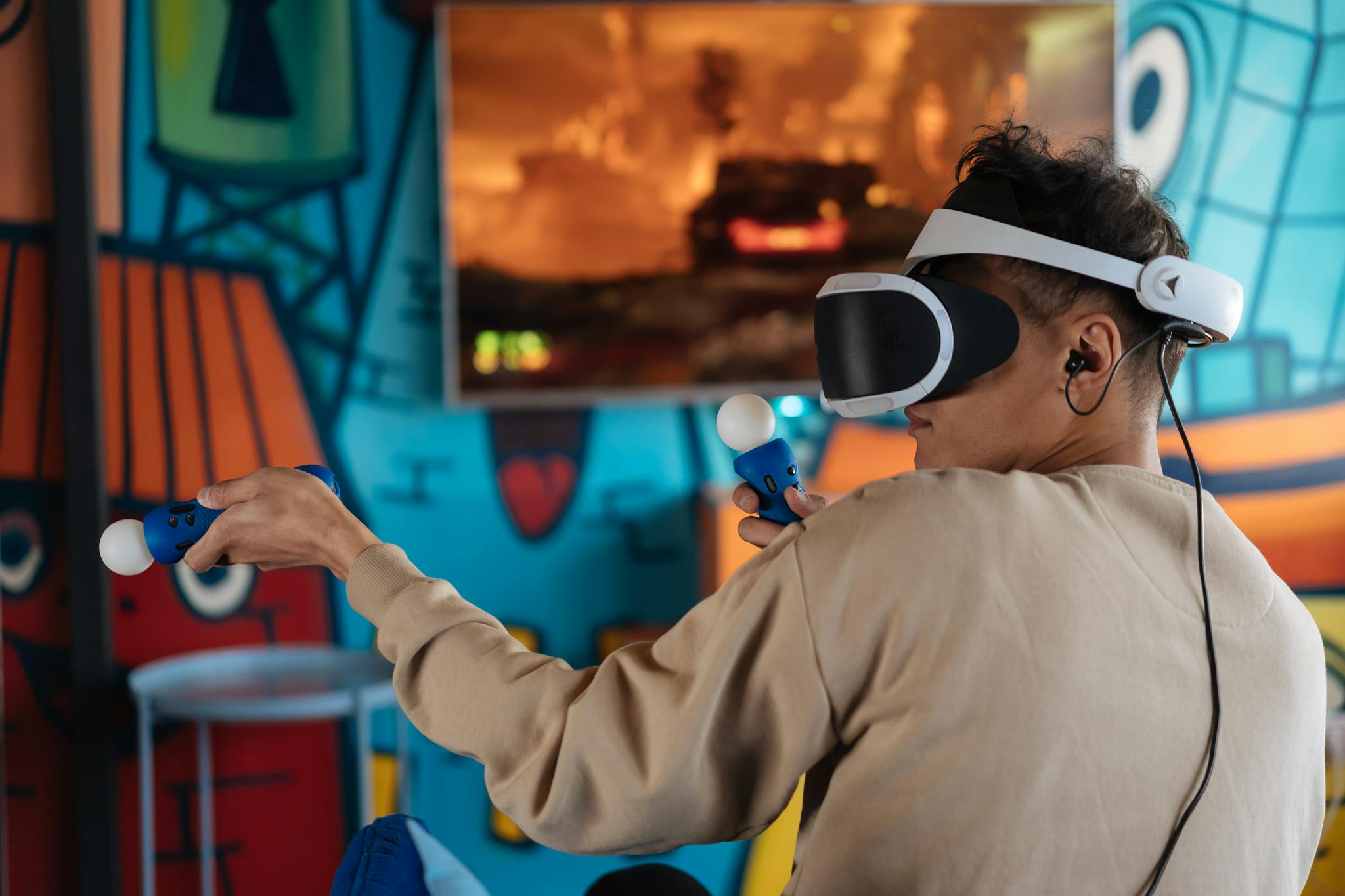 Person enjoying virtual reality gaming with VR headset and controllers in a vibrant room.